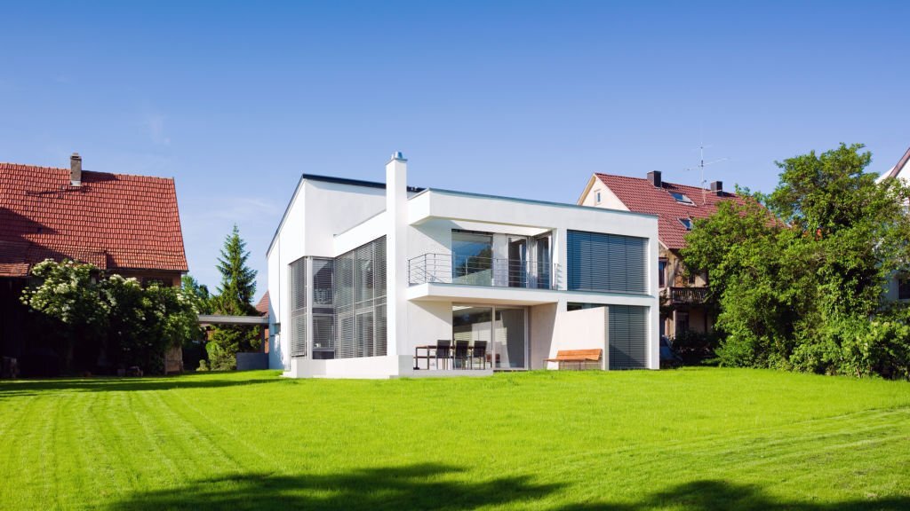 Modern Architecture Sustainable Green Home Panorama with Summer Garden Meadow Front Yard under blue cloudless summer sky.